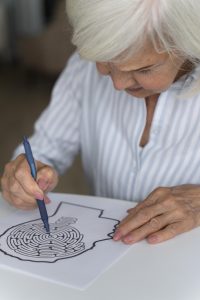 Mujer realizando una tarea de rehabilitación tras un ictus, trazando con lápiz el camino de un laberinto en un papel con una silueta de cabeza.