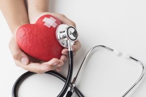 Manos sosteniendo un corazón simbólico con un parche y un estetoscopio, representando la atención y rehabilitación tras un problema cardíaco.