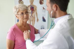Mujer mayor siendo auscultada por un médico durante una consulta, reflejando desigualdades en el acceso a la rehabilitación cardíaca.