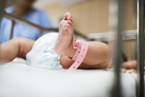 Recién nacido en una cuna hospitalaria con pulsera identificativa rosa, símbolo de la atención neonatal.