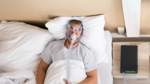 Hombre dormido con mascarilla CPAP, tratamiento habitual para la apnea del sueño, en cama.