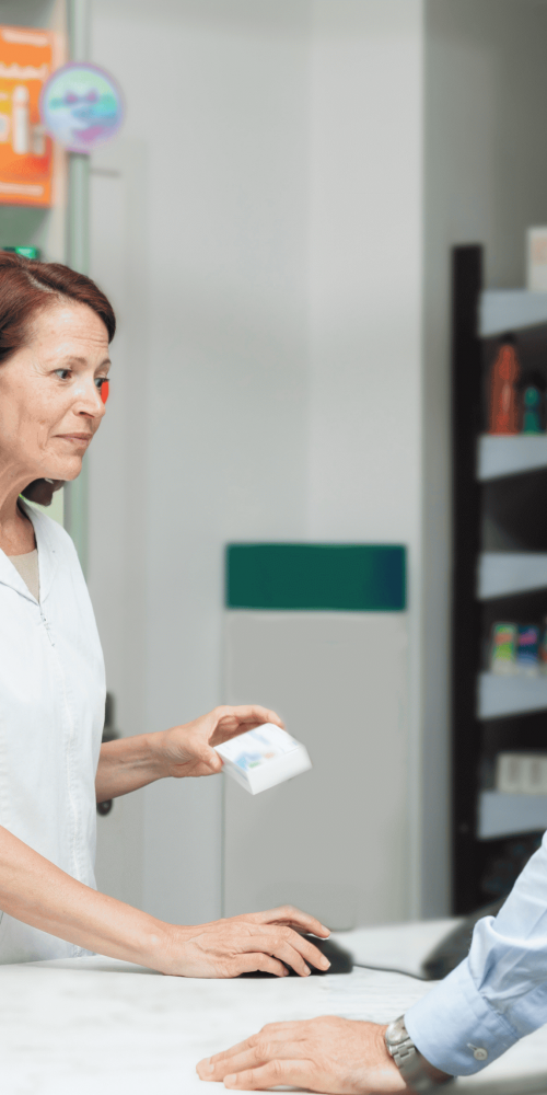 Farmacéutica atiende a un paciente en una farmacia, entregando un medicamento como parte de la atención en salud.