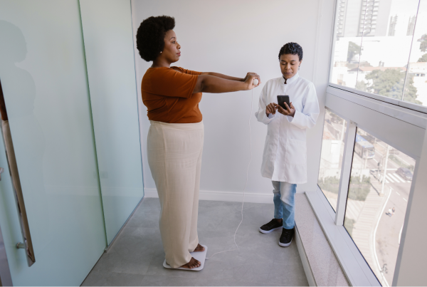 Mujer midiendo su composición corporal con una bascula por la bioimpedancia. Medico que revisa los datos.