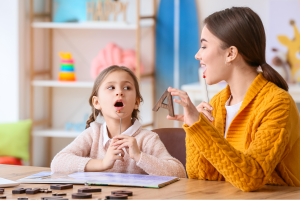Niña en sesión de logopedia con una profesional, aprendiendo a pronunciar sonidos como parte del tratamiento de la tartamudez, en el contexto del Día Internacional de la Tartamudez.