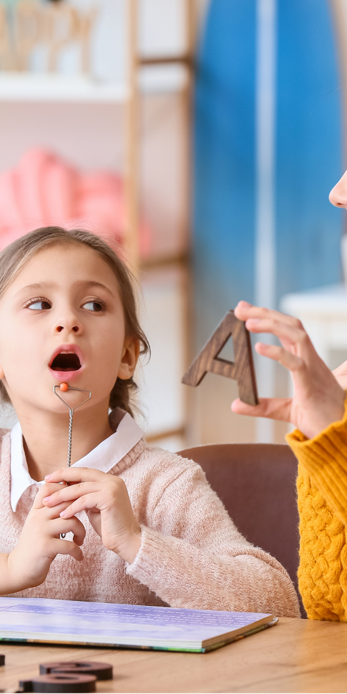Niña en sesión de logopedia con una profesional, aprendiendo a pronunciar sonidos como parte del tratamiento de la tartamudez, en el contexto del Día Internacional de la Tartamudez.