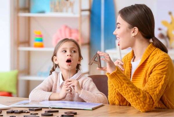 Niña en sesión de logopedia con una profesional, aprendiendo a pronunciar sonidos como parte del tratamiento de la tartamudez, en el contexto del Día Internacional de la Tartamudez.