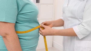 Profesional de la salud midiendo la cintura de una persona con obesidad y sobrepeso con una cinta métrica.