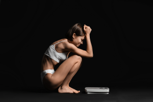 Mujer sentada junto a una báscula, con gesto de angustia, representando la lucha emocional detrás de los Trastornos de la Conducta Alimentaria en el Día Internacional TCA.