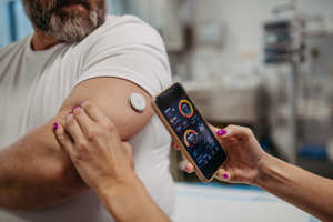 Persona utilizando un sensor en el brazo para monitorizar su glucosa y consultando los datos en una aplicación móvil, como parte del control de la diabetes.