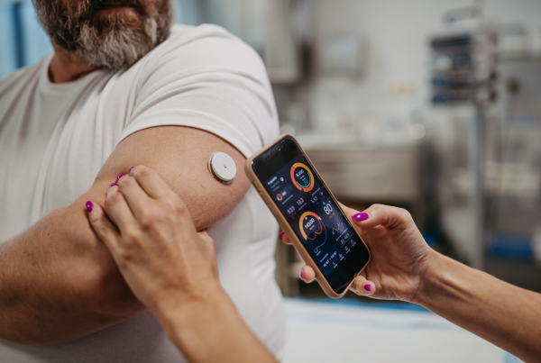 Persona utilizando un sensor en el brazo para monitorizar su glucosa y consultando los datos en una aplicación móvil, como parte del control de la diabetes.