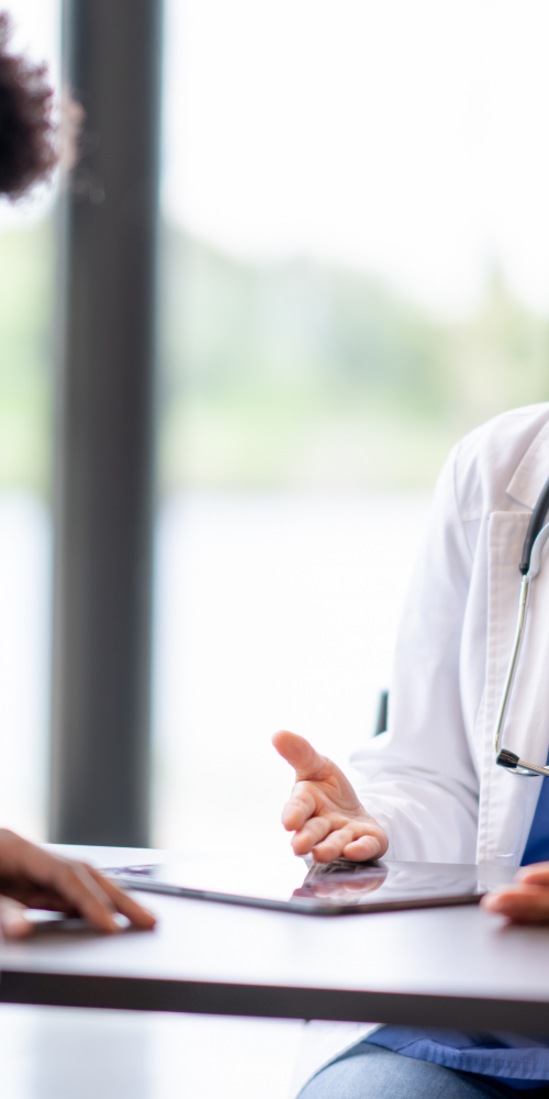 Profesional sanitaria conversa con un paciente durante una consulta médica, explicando información para ayudarle a comprender su diagnóstico y tomar decisiones informadas sobre su salud