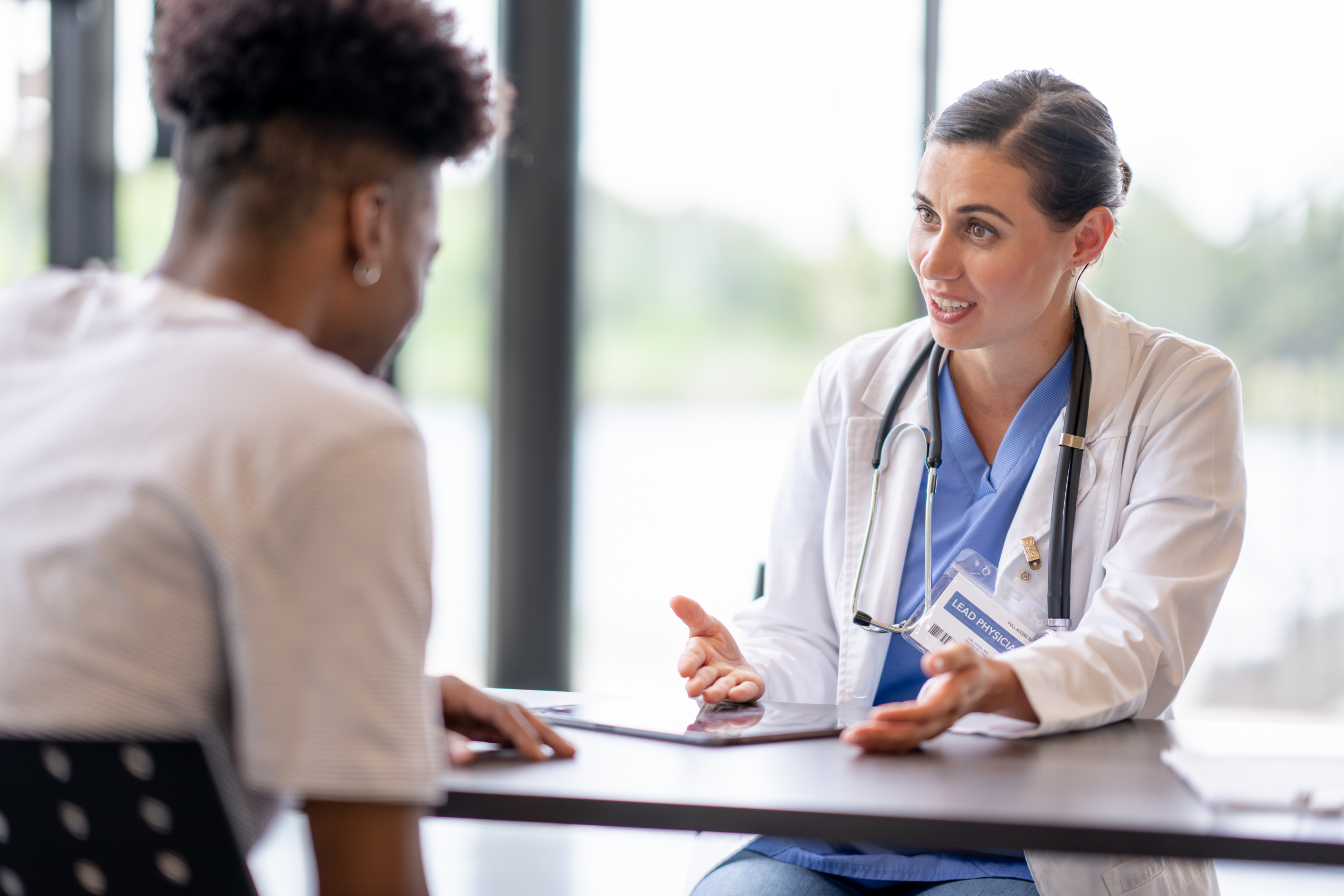 Profesional sanitaria conversa con un paciente durante una consulta médica, explicando información para ayudarle a comprender su diagnóstico y tomar decisiones informadas sobre su salud