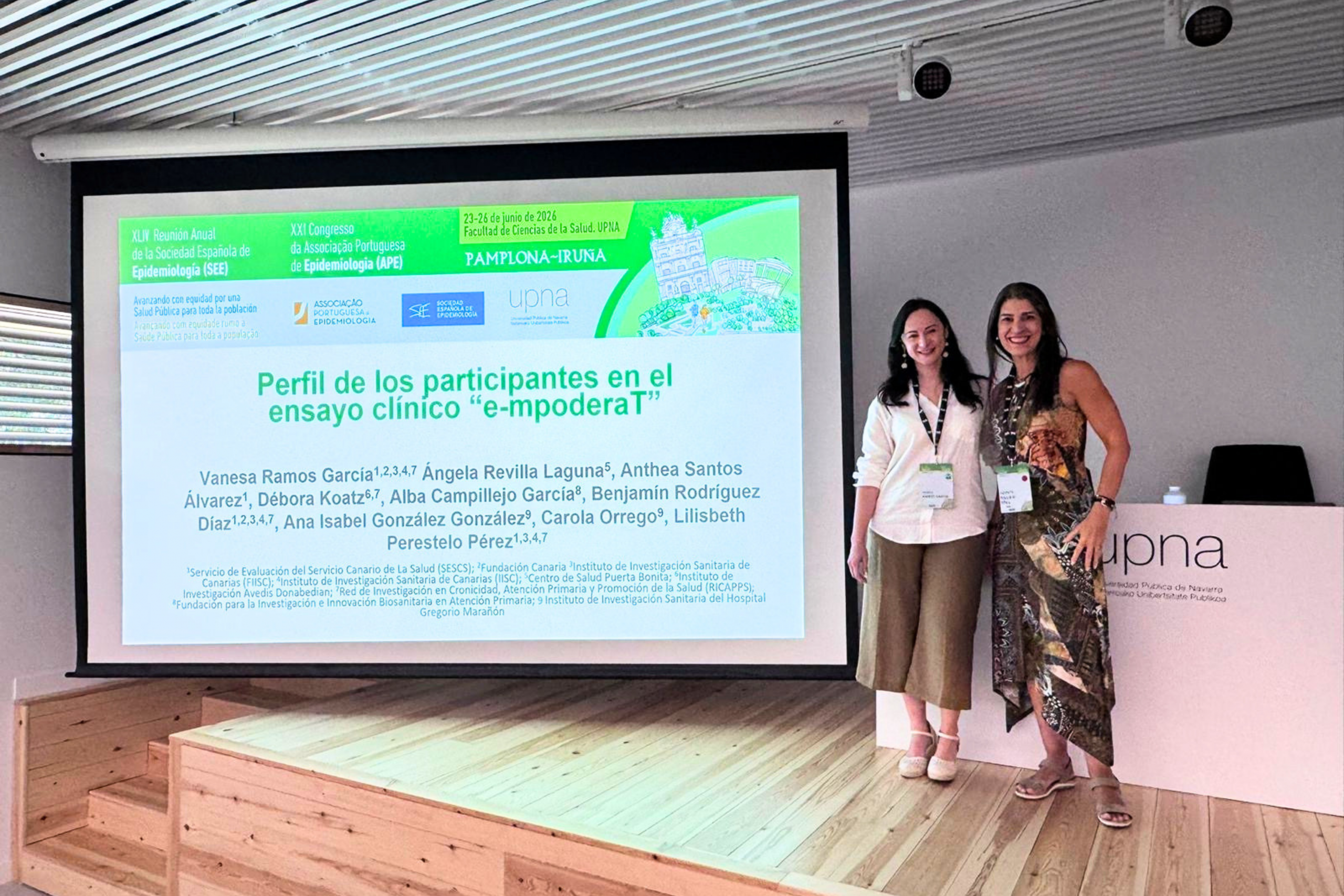 Vanesa Ramos García y Lilisbeth Perestelo-Pérez junto a la diapositiva del ensayo clínico e-mpoderaT durante la Reunión Anual SEE 2026, celebrada en la Universidad Pública de Navarra.