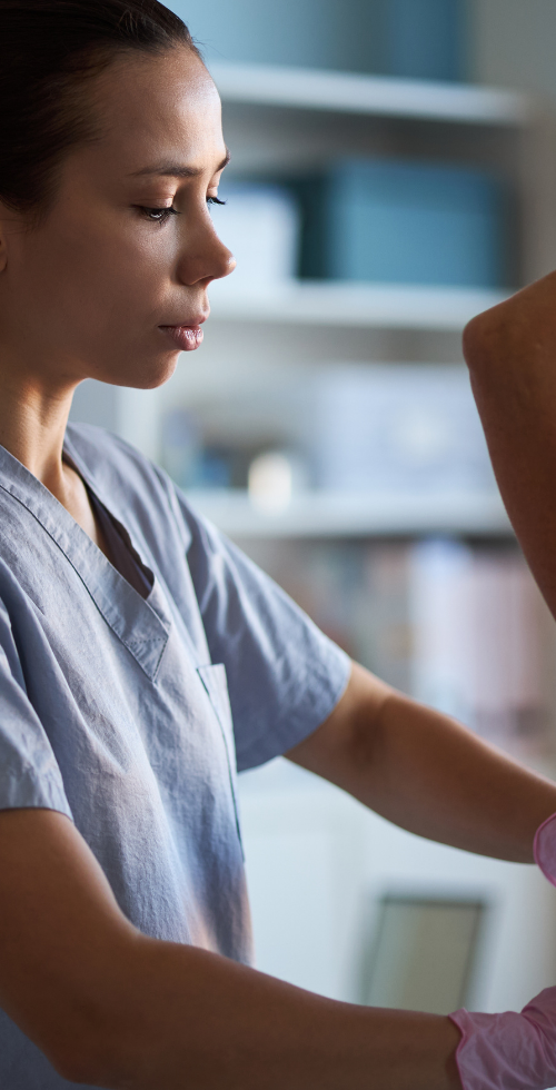 Profesional sanitaria con guantes realizando una exploración clínica mamaria a una paciente en una consulta médica, como parte del proceso diagnóstico del cáncer de mama.