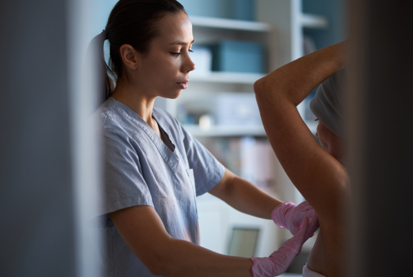 Profesional sanitaria con guantes realizando una exploración clínica mamaria a una paciente en una consulta médica, como parte del proceso diagnóstico del cáncer de mama.