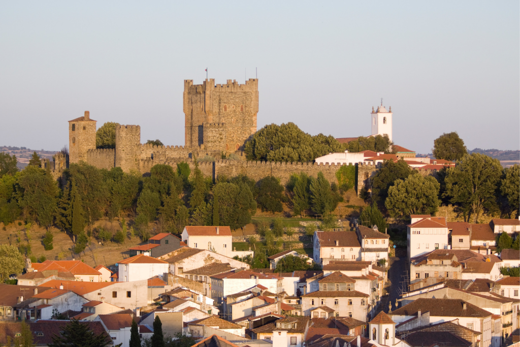 Castillo medieval de Bragança (Portugal), con su gran torre del homenaje y la muralla rodeada de árboles, sobre las casas blancas de tejados rojos del casco histórico.